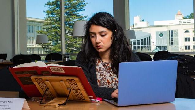 Student studies with a book and a laptop in the library.